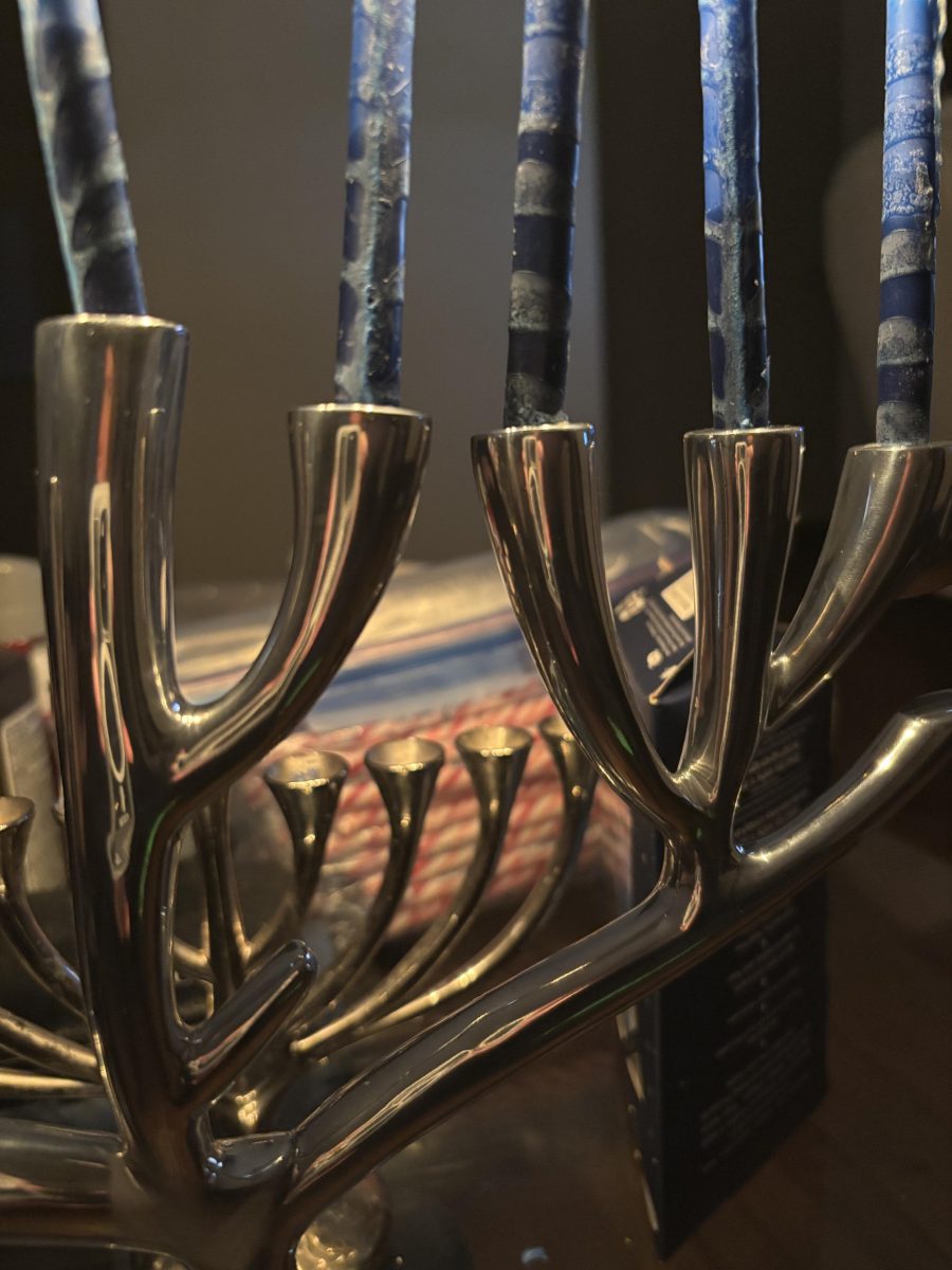 Beaten metal menorah with eight lit candles. Thre on the left, shamash in the middle, and four on the right.